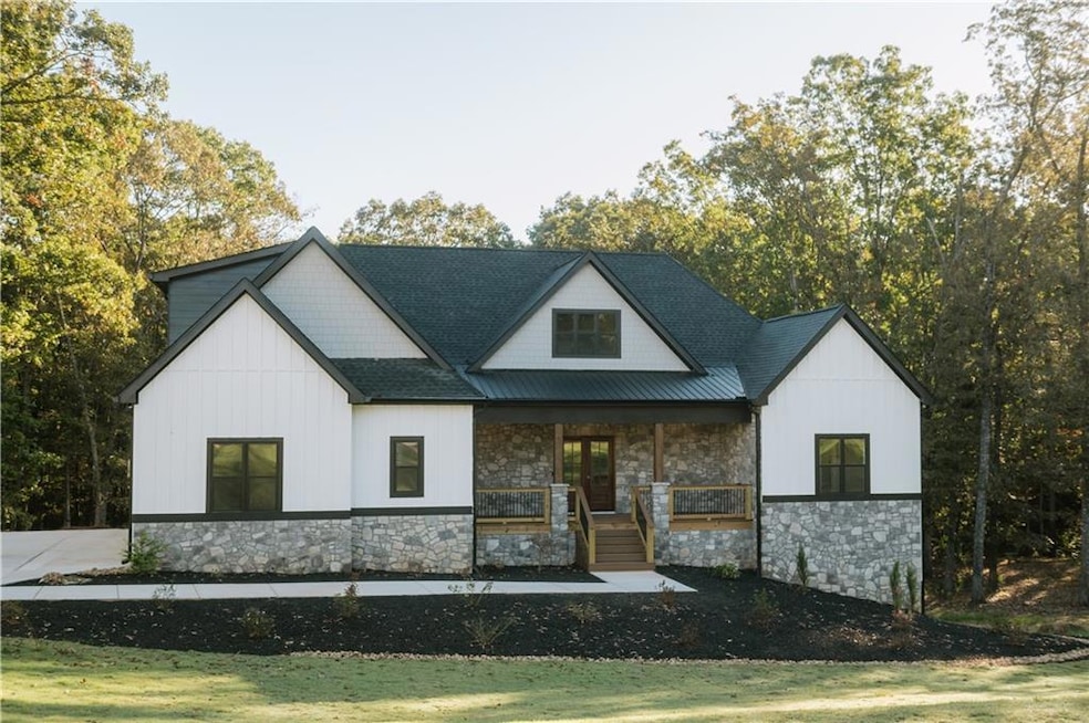 Modern farmhouse style home with a porch, board and batten siding, stone siding, and a shingled roof