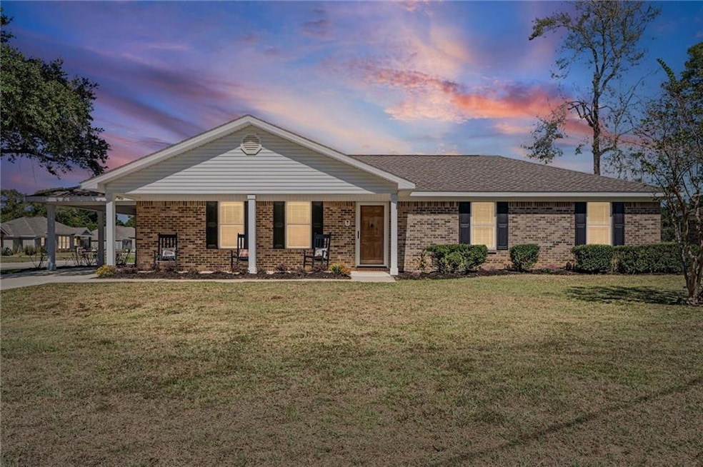 View of front of house with a porch, a lawn, brick siding, a carport, and roof with shingles
