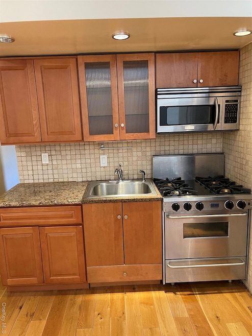 Kitchen featuring range, stainless steel microwave, glass insert cabinets, and brown cabinets