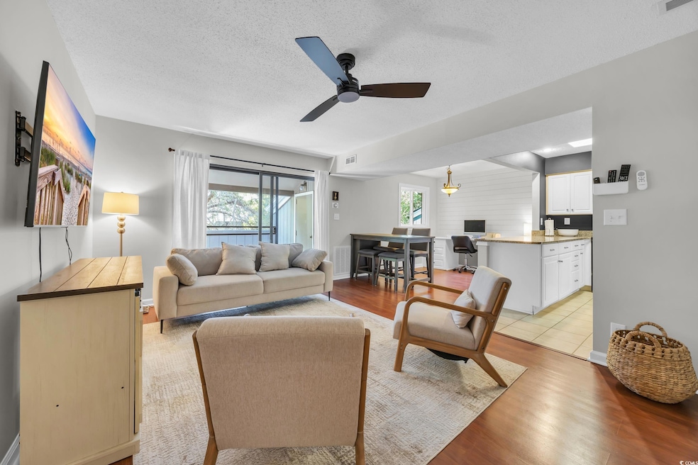 Living room featuring a ceiling fan, light wood-type flooring, and a textured ceiling