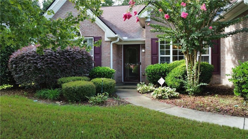 View of exterior entry featuring brick siding, roof with shingles, and a yard