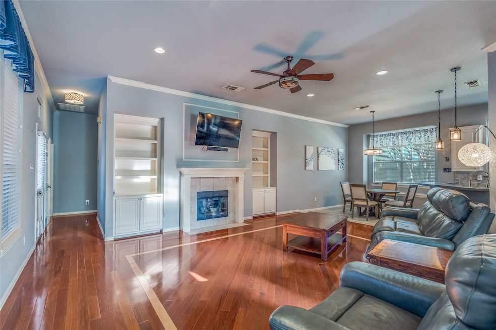 Living room with crown molding, built in features, a ceiling fan, a tiled fireplace, and hardwood / wood-style floors