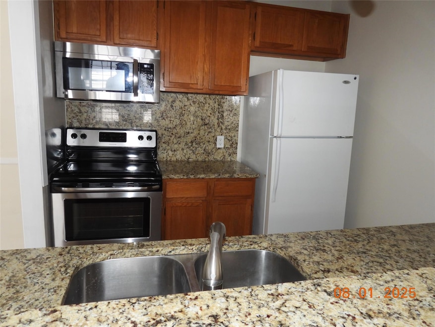 Kitchen with appliances with stainless steel finishes, backsplash, brown cabinetry, and light stone counters