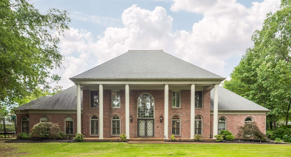 Greek revival inspired property with a shingled roof, a front yard, and brick siding