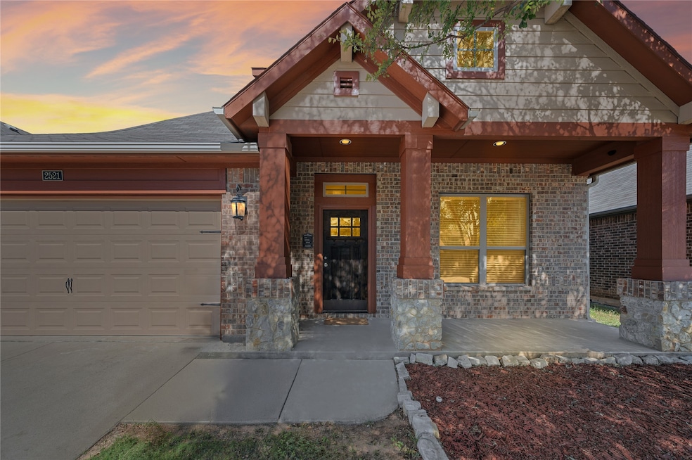 Exterior entry at dusk featuring covered porch, a garage, concrete driveway, and brick siding