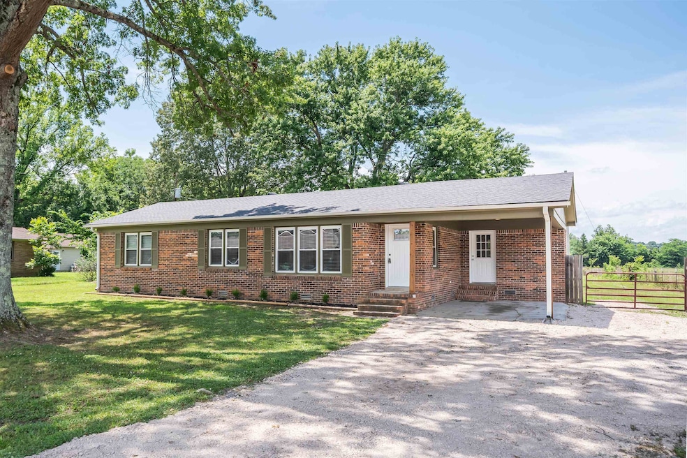 Ranch-style home featuring brick siding, driveway, a shingled roof, and a carport