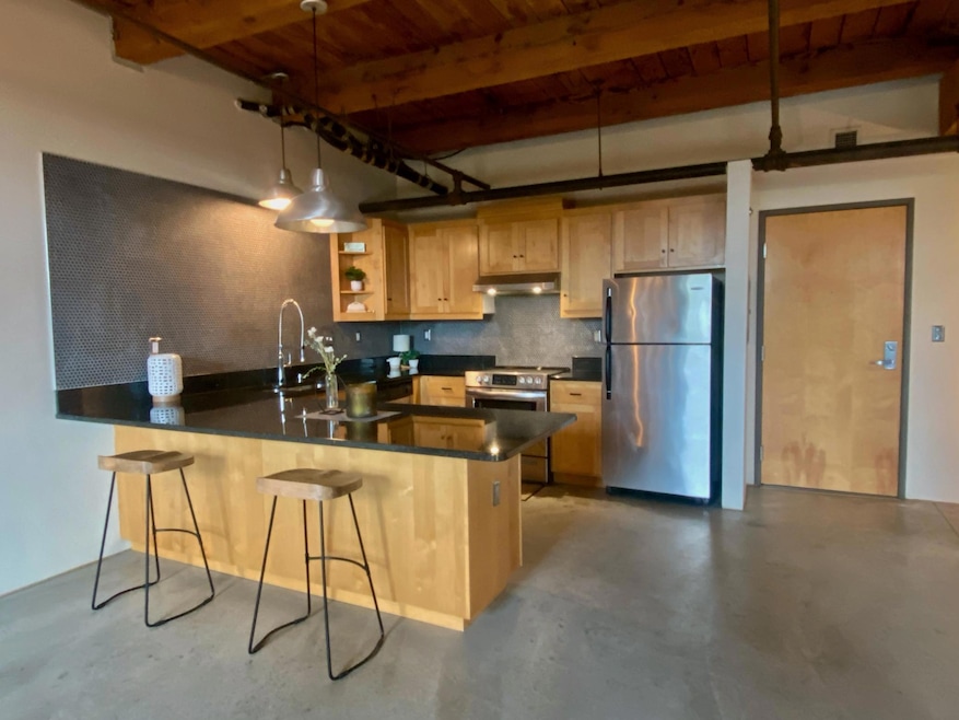 Welcome to #205 in Calumet Lofts! The large kitchen in this large, open loft features a matching stainless steel appliance package,  coordinated industrial pendant lighting, and a huge peninsula with seating for at least four.
