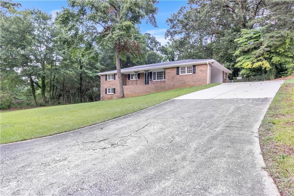 Ranch-style home featuring asphalt driveway, brick siding, a front lawn, and view of scattered trees