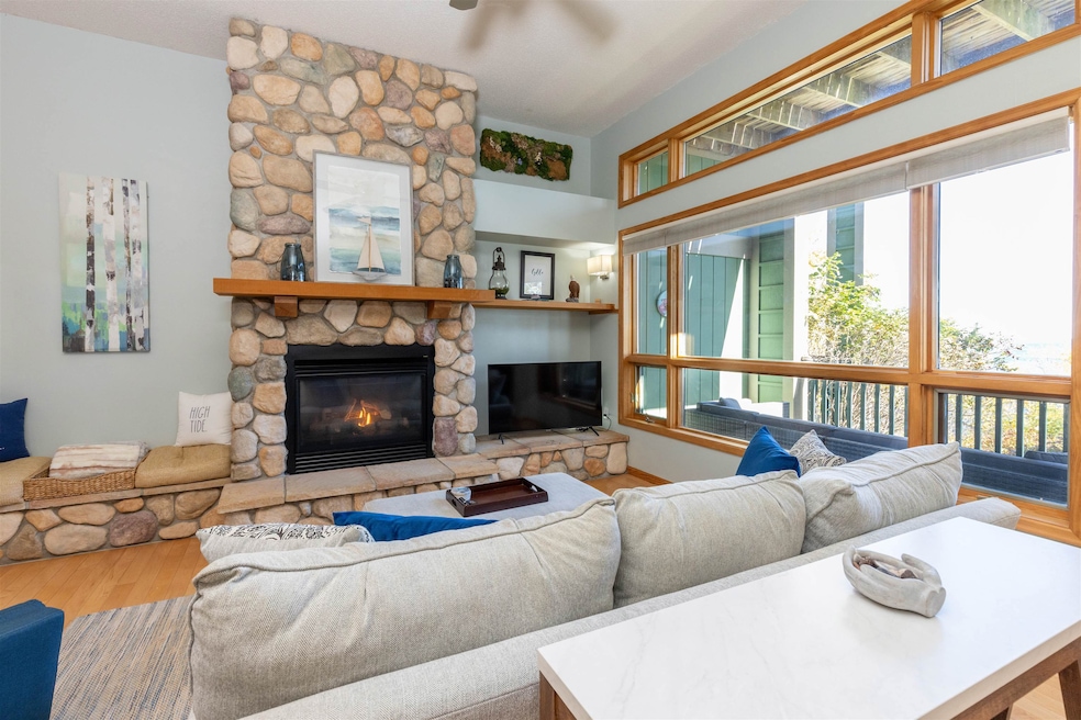 Living room with wood finished floors, a stone fireplace, and ceiling fan