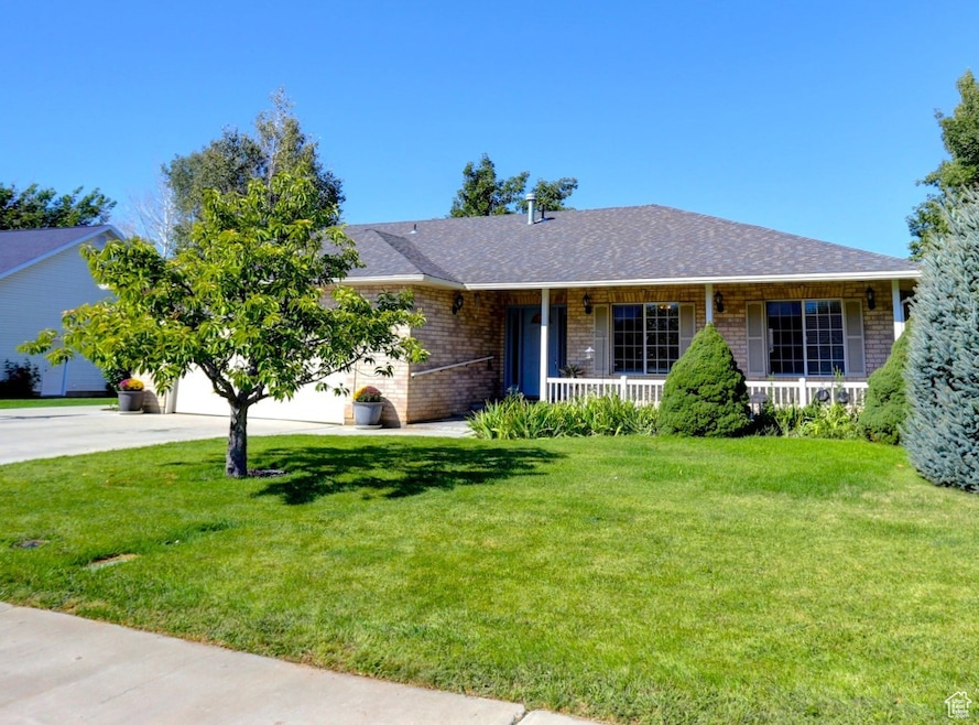 Ranch-style house with a porch, brick siding, a front lawn, concrete driveway, and a shingled roof
