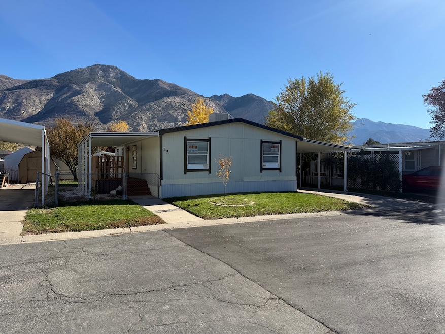 Manufactured / mobile home featuring an attached carport, a mountain view, a front lawn, and an outbuilding