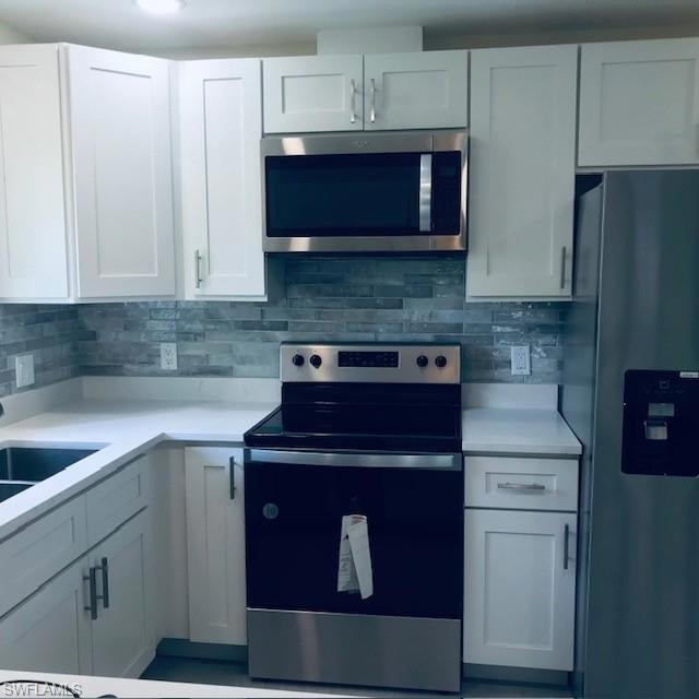 Kitchen with appliances with stainless steel finishes, white cabinets, tasteful backsplash, and light stone countertops