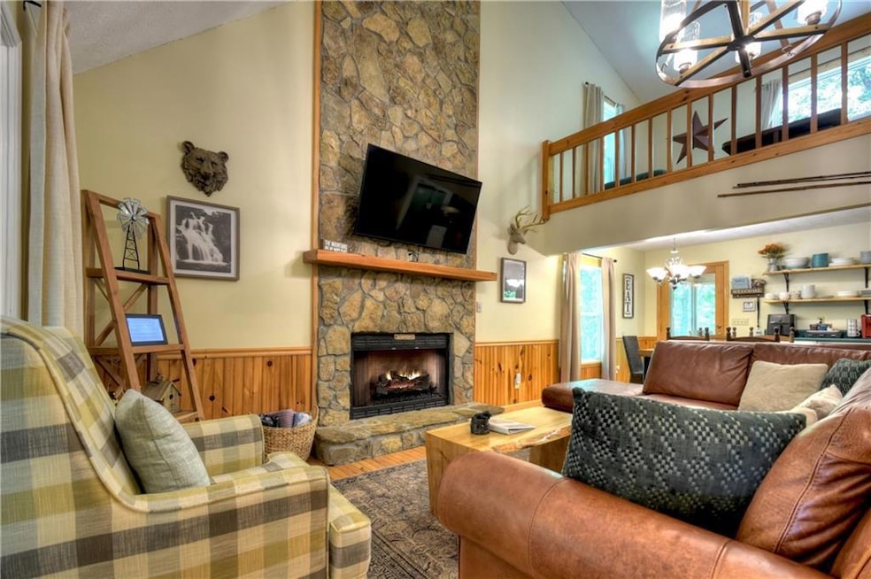 Living room with a chandelier, wood finished floors, a wainscoted wall, a stone fireplace, and high vaulted ceiling