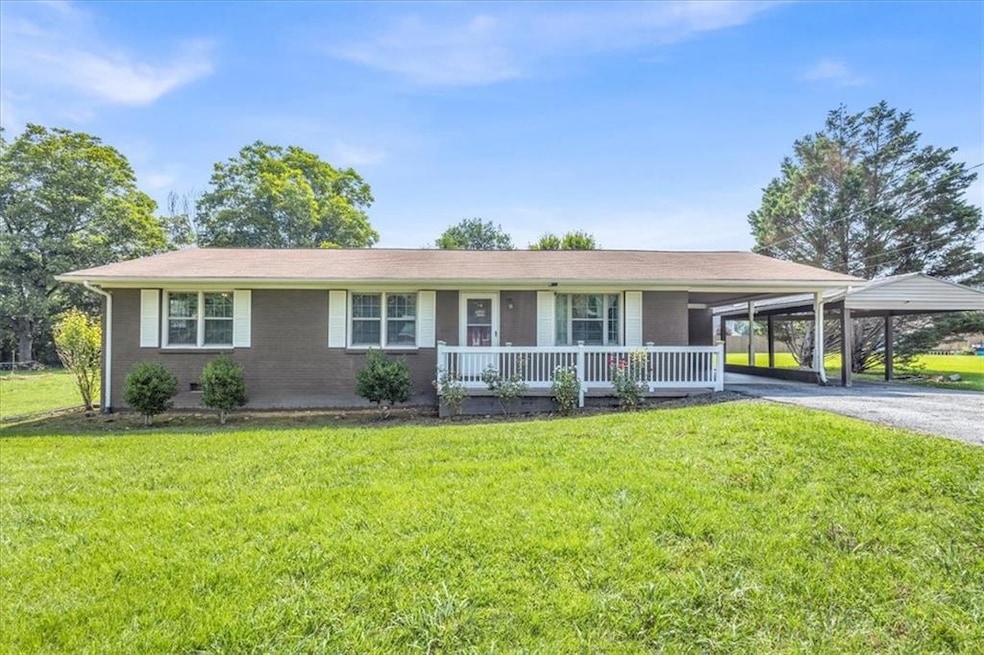 Ranch-style house featuring covered porch, a front yard, driveway, an attached carport, and brick siding