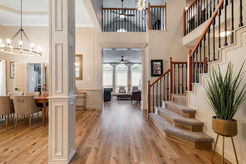 Foyer featuring ornate columns, LVP / wood-type flooring, ceiling fan with notable chandelier, a high ceiling, and ornamental molding