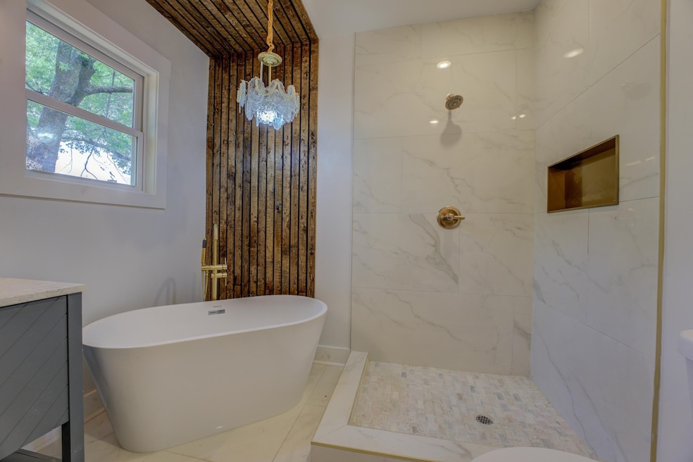 Bathroom with a freestanding bath, a marble finish shower, and vanity