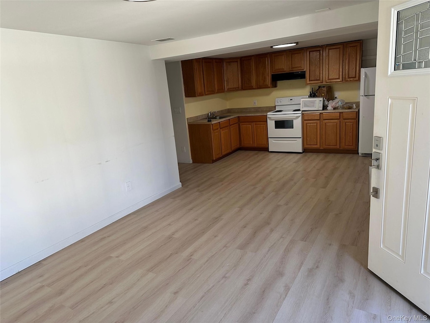 Kitchen featuring white appliances, brown cabinetry, light wood finished floors, and under cabinet range hood