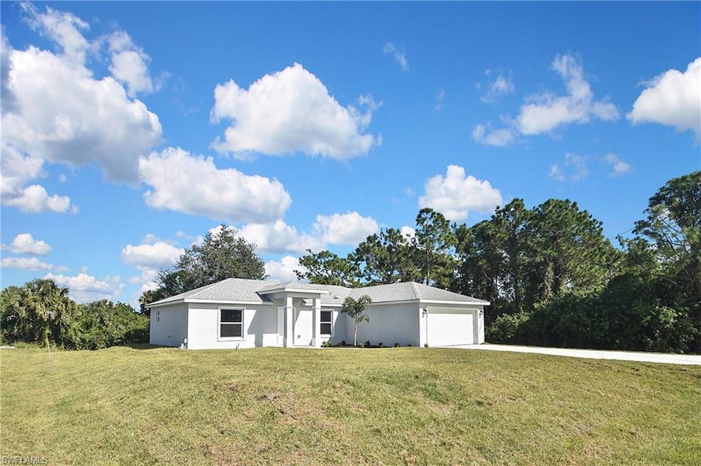 View of front of house with a front yard, stucco siding, an attached garage, concrete driveway, and view of scattered trees