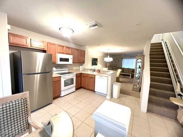 Kitchen featuring a sink, open floor plan, white appliances, a peninsula, and light countertops