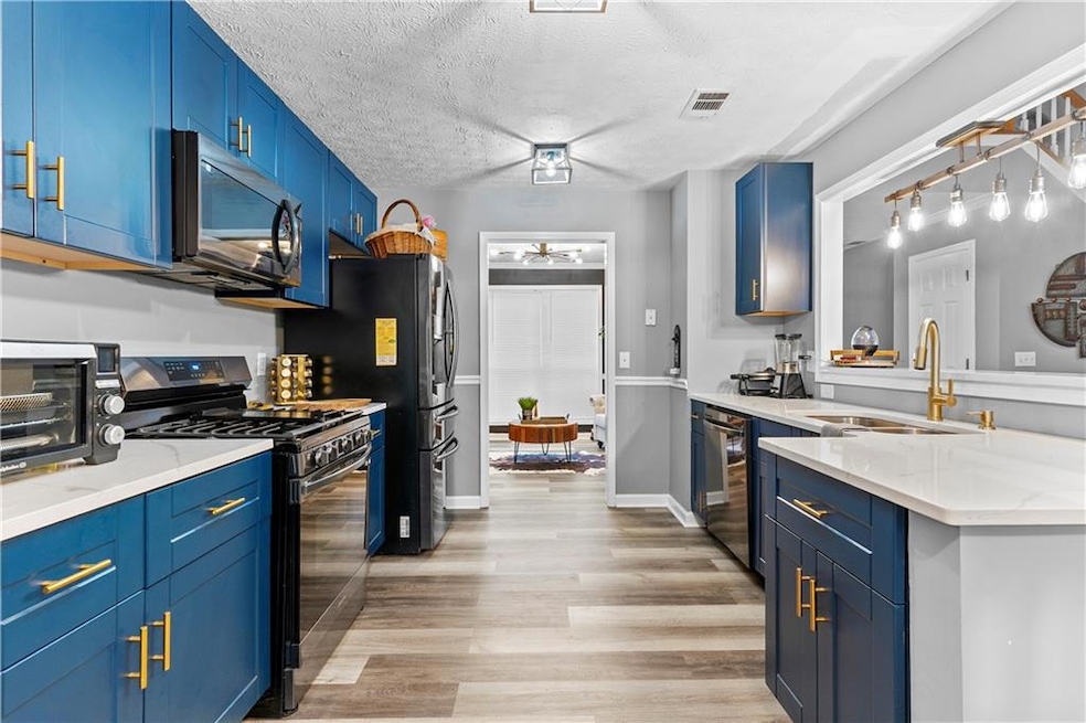 Kitchen featuring appliances with stainless steel finishes, blue cabinets, light wood-style floors, a ceiling fan, and light stone countertops