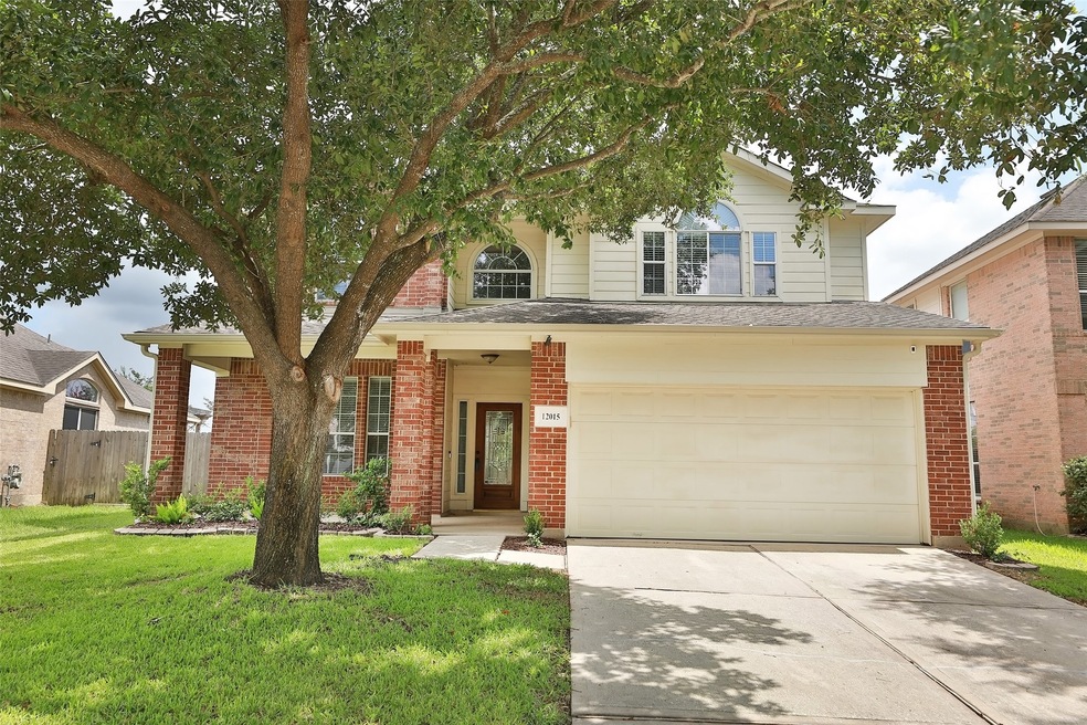 Two-story suburban house with a red brick, large covered porch, and a front lawn with a mature tree.