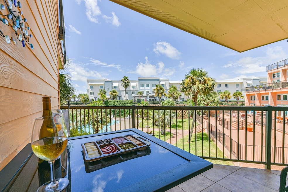 A cozy balcony with a table set for relaxation awaits. The view from this adorable condo overlooks the newly renovated resort pool surrounded by palm trees and lush landscaping. Ideal for enjoying outdoor leisure!