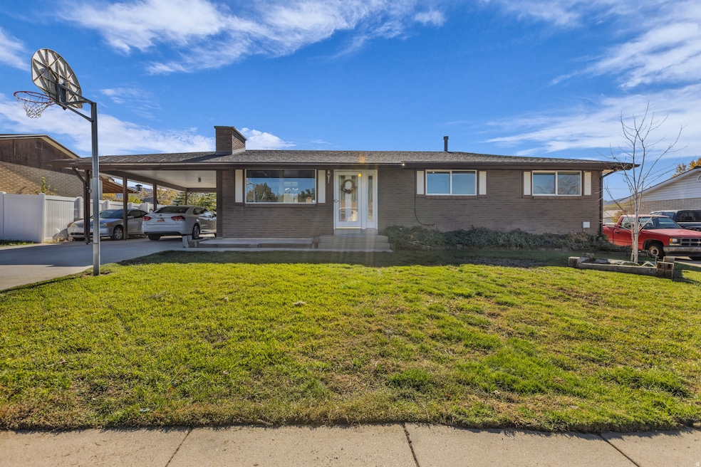 Ranch-style home featuring an attached carport, brick siding, a front yard, a chimney, and driveway