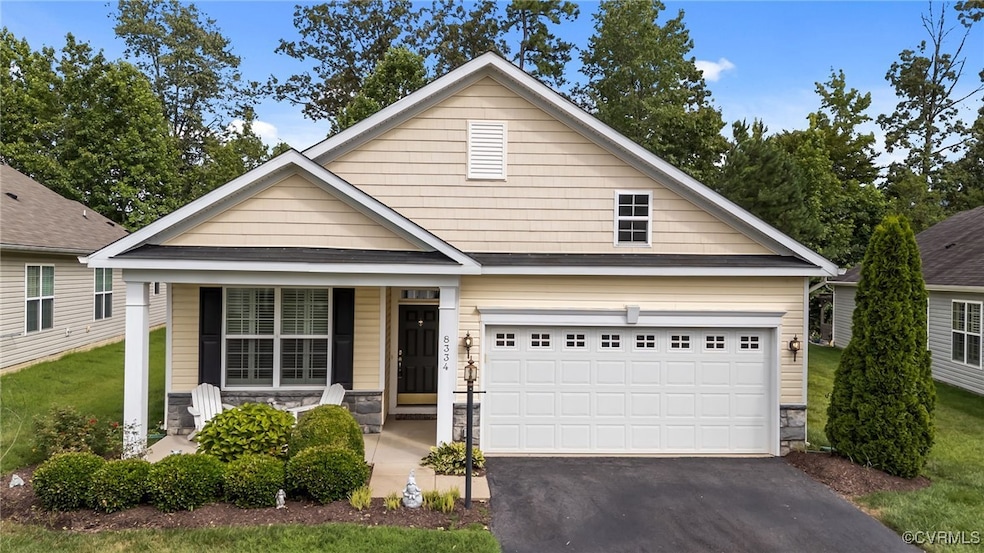 View of front of house featuring covered porch, asphalt driveway, stone siding, a front lawn, and a garage