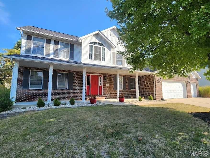 View of front of home with a front yard, brick siding, covered porch, and driveway