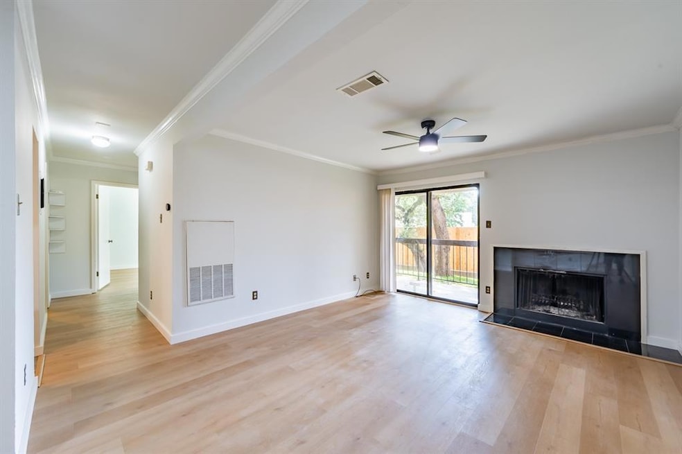 Unfurnished living room featuring ornamental molding, a fireplace with raised hearth, light wood-style floors, and ceiling fan