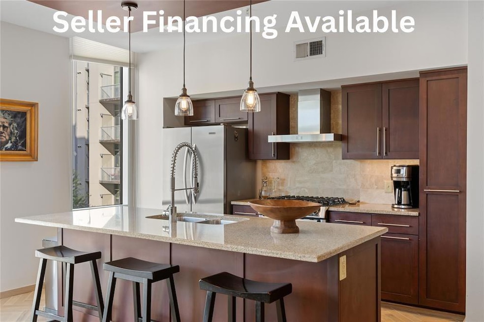 Kitchen with light stone countertops, wall chimney range hood, decorative light fixtures, tasteful backsplash, and stainless steel appliances