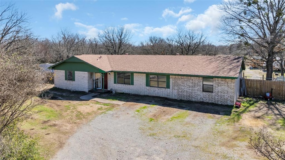 Ranch-style house with brick siding, dirt driveway, and a shingled roof