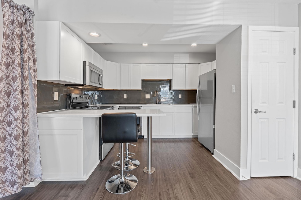 Kitchen featuring white cabinetry, backsplash, stainless steel appliances, dark wood-style flooring, and recessed lighting