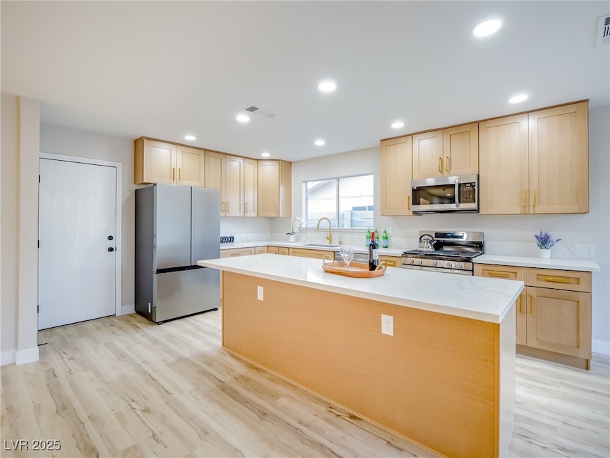 Kitchen with light brown cabinetry, stainless steel appliances, a center island, and recessed lighting