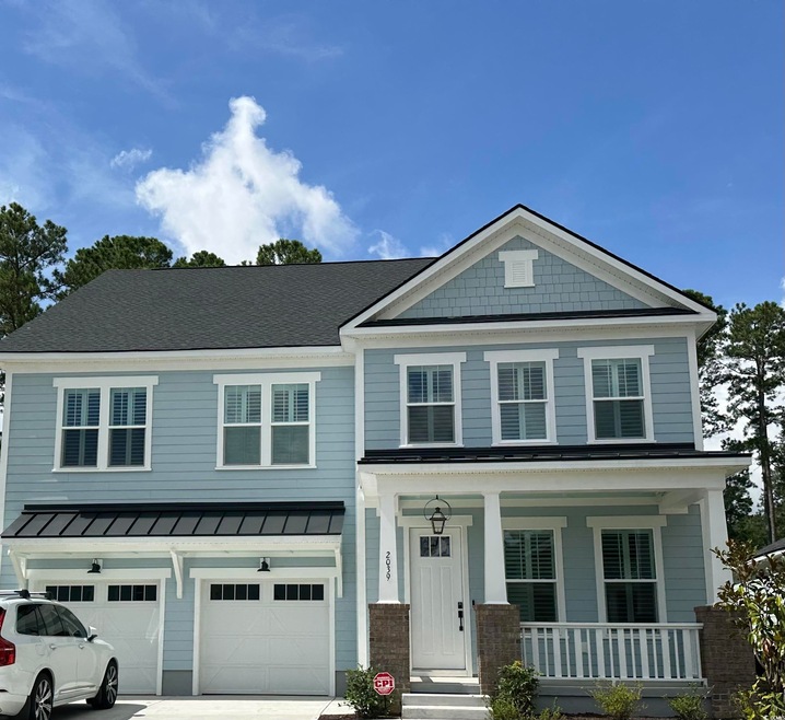 View of front of house featuring a porch, an attached garage, concrete driveway, a standing seam roof, and a metal roof
