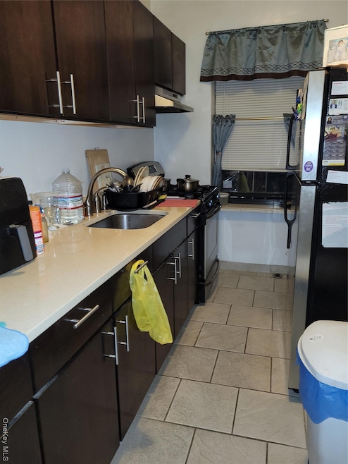 Kitchen with refrigerator, light tile patterned floors, black range with gas stovetop, extractor fan, and light stone countertops