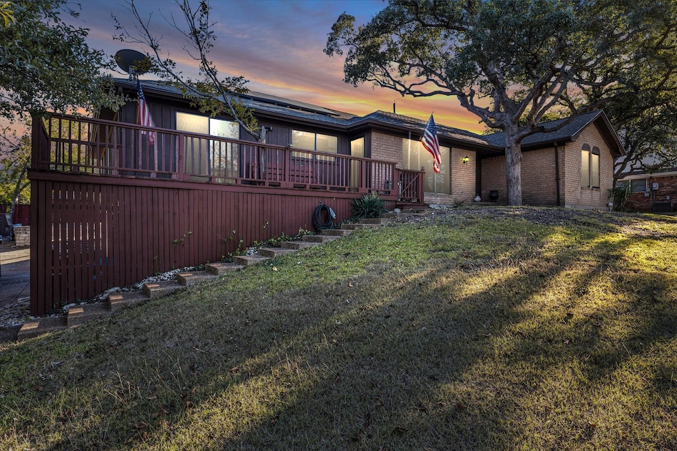 Back of house at dusk featuring solar panels, brick siding, a deck, and a lawn