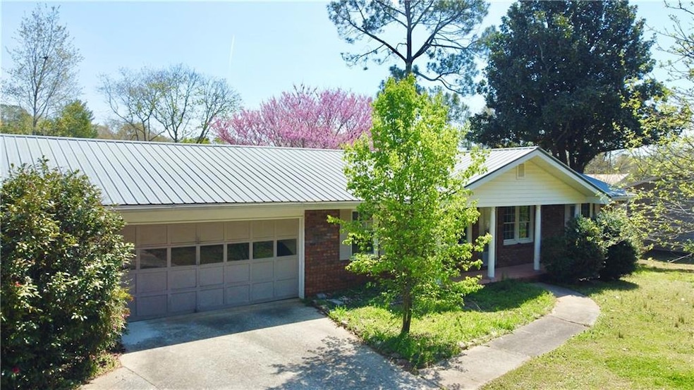 Ranch-style house with brick siding, a front yard, a garage, and metal roof