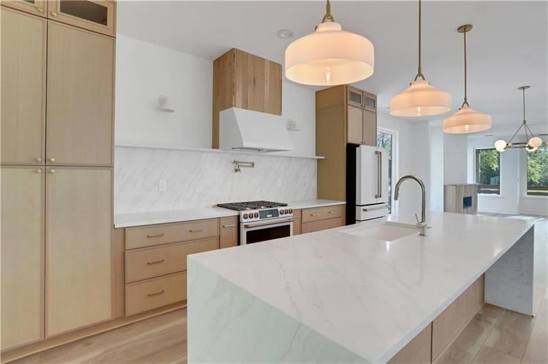 Kitchen with glass insert cabinets, light brown cabinets, high quality appliances, and light stone countertops