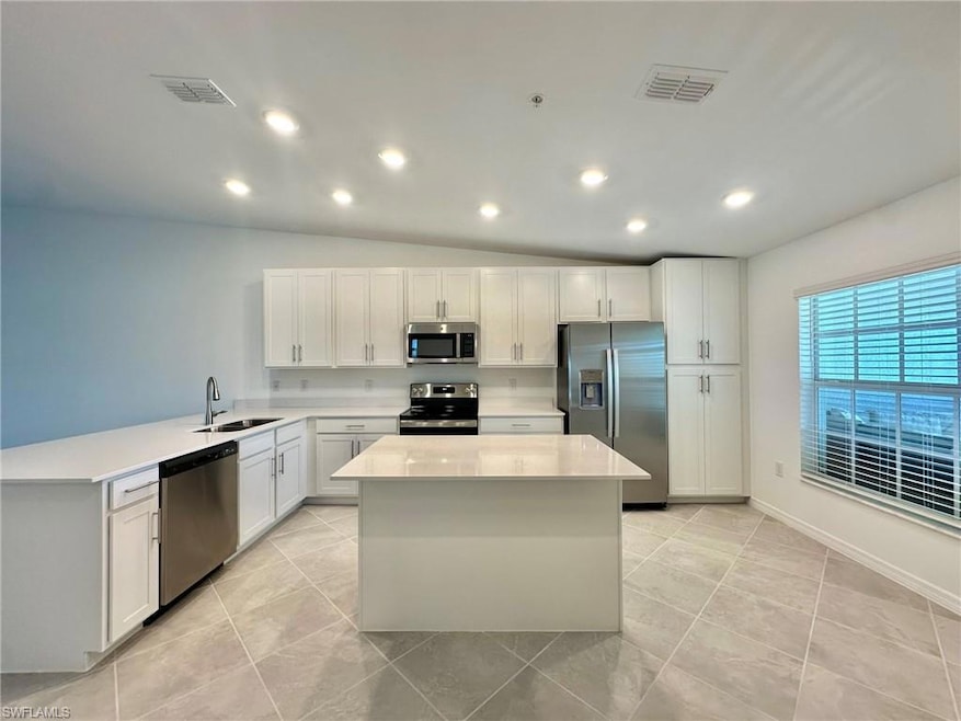 Kitchen featuring a kitchen island, stainless steel appliances, lofted ceiling, and sink.