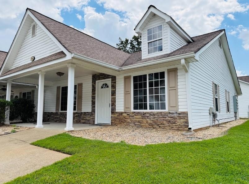 View of front facade with stone siding, a shingled roof, covered porch, and a front yard