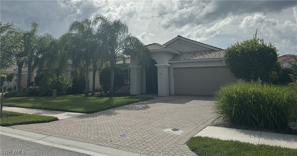 Ranch-style home with a garage, paver driveway, a tile roof, a front lawn, and stucco siding