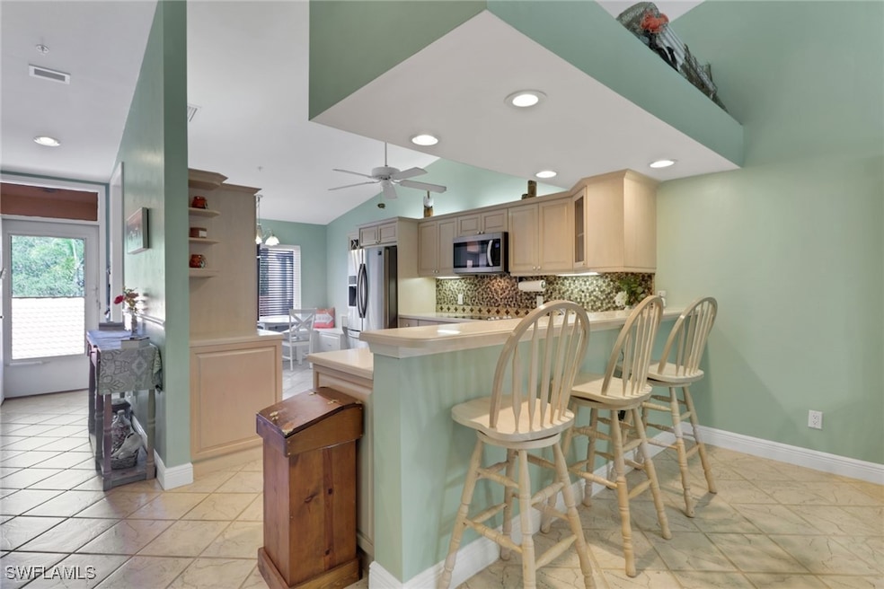 Kitchen with tasteful backsplash, a kitchen breakfast bar, stainless steel appliances, light countertops, and lofted ceiling