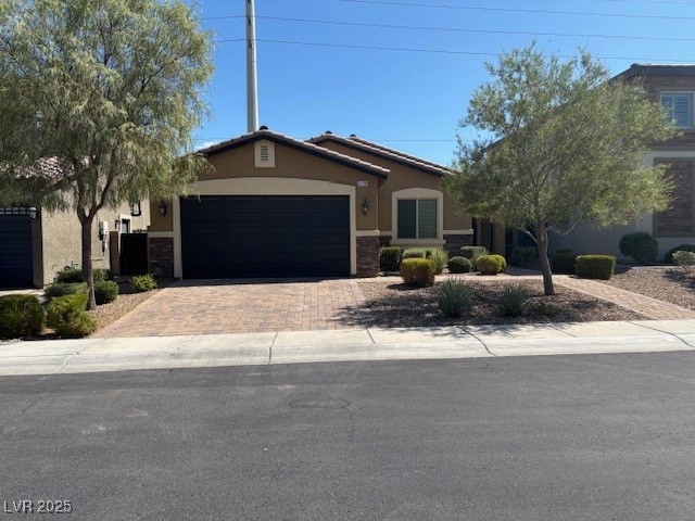 Single story home featuring stucco siding, decorative driveway, a garage, and stone siding
