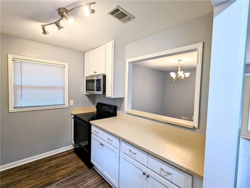 Kitchen featuring black range with electric stovetop, stainless steel microwave, white cabinetry, a chandelier, and dark wood-style floors