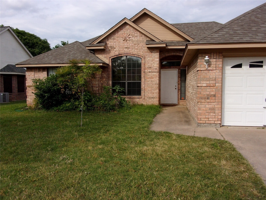 View of front of home with brick siding, a front yard, a shingled roof, and an attached garage