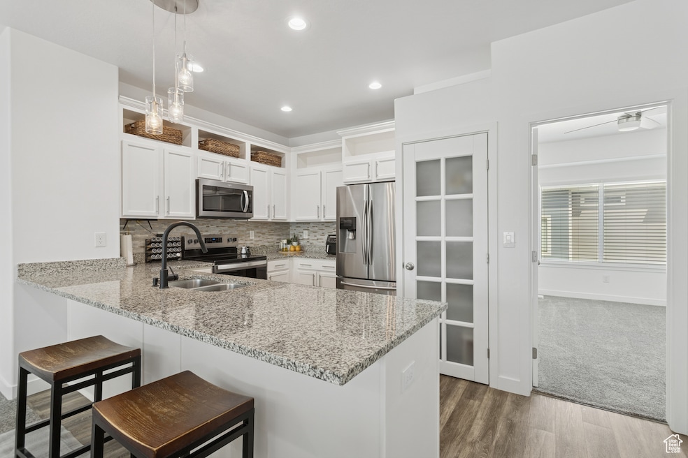 Kitchen with white cabinetry, tasteful backsplash, stainless steel appliances, light stone countertops, and a peninsula