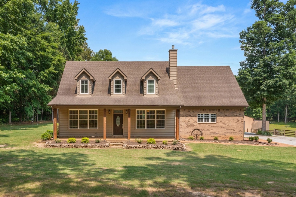 Cape cod-style house with a chimney, covered porch, a front yard, roof with shingles, and brick siding