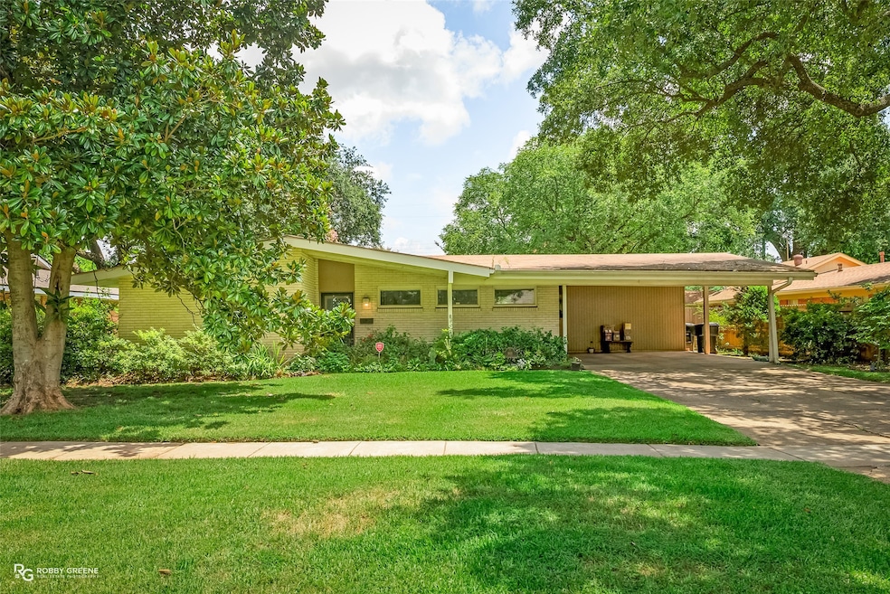 View of front facade with a carport, brick siding, concrete driveway, and a front yard