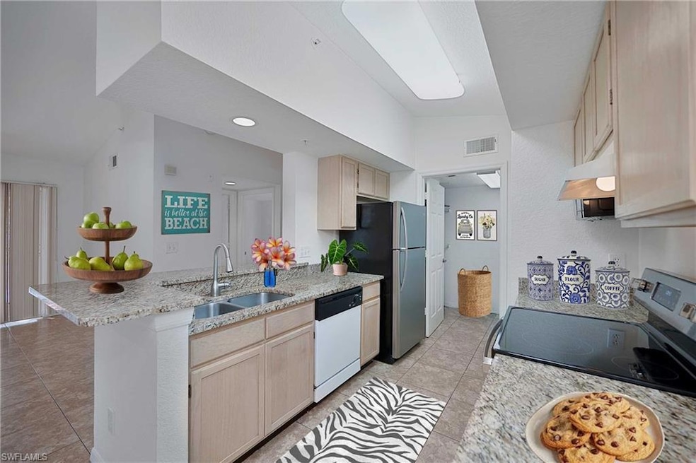 Kitchen featuring stainless steel appliances, a sink, a peninsula, vaulted ceiling, and light tile patterned floors